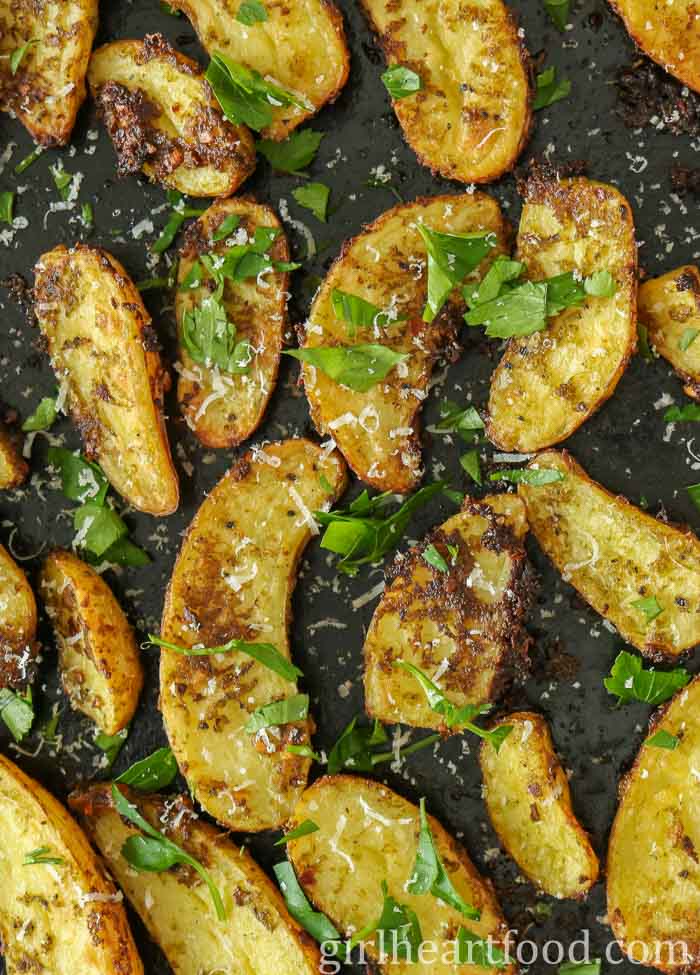 Roasted pesto potatoes on a sheet pan with fresh parsley and Parmesan over top.