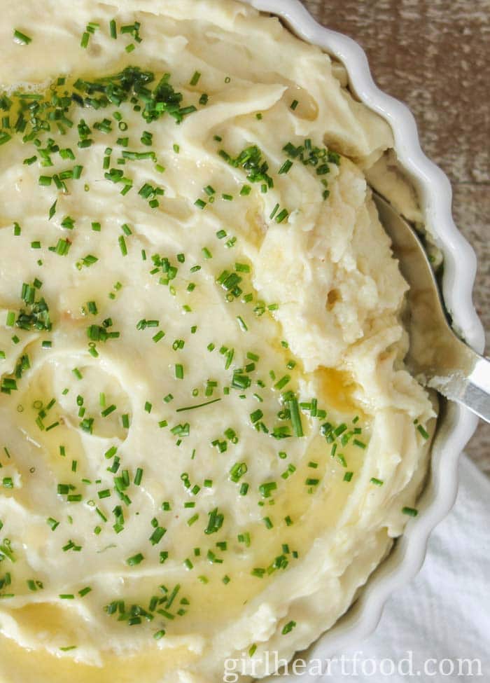 Close-up of a dish of garlic mashed potatoes with a serving spoon dunked into it.
