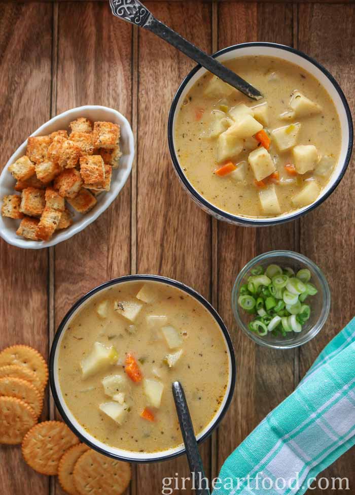 Two bowls of celery root soup alongside croutons, crackers, and a dish of green onion.