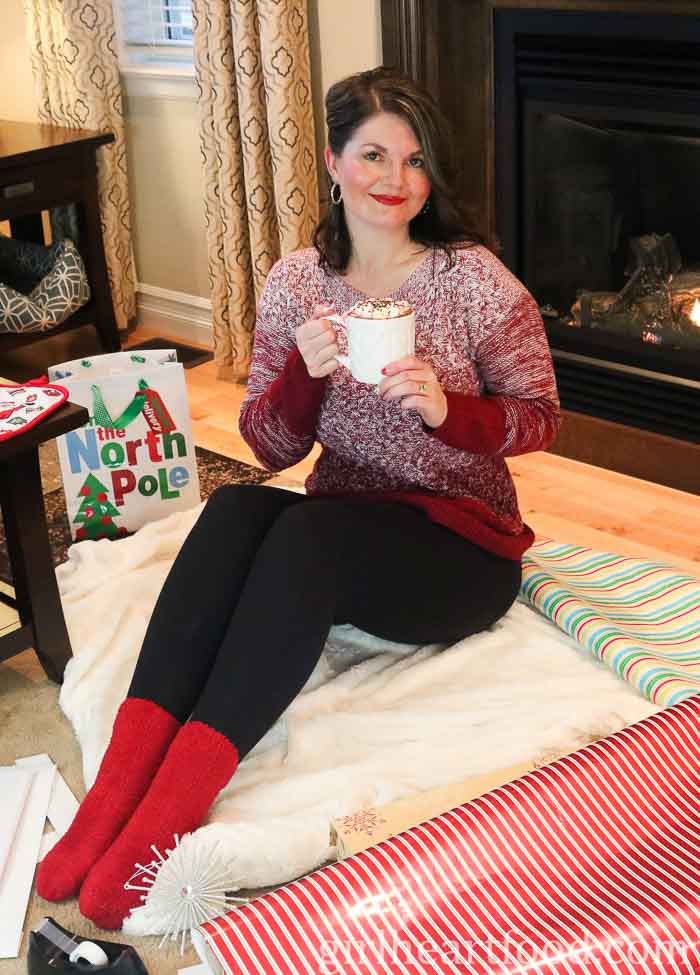 Woman holding a mug of hot chocolate, sitting alongside wrapping paper.