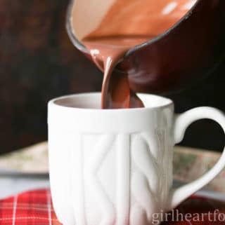 Pouring dark hot chocolate from a pot to a white mug.