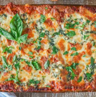 Homemade lasagna in a baking dish garnished with basil and parsley.