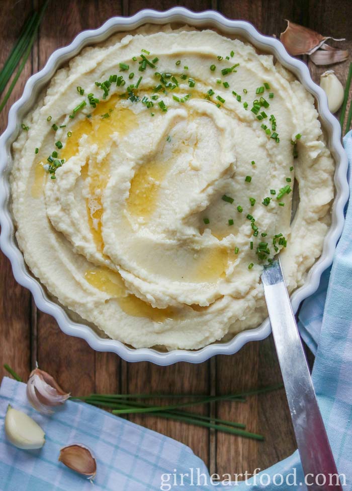 Pureed celery root in a dish with a serving spoon, garnished with butter and chives.