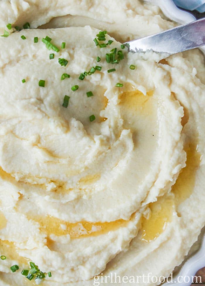 Close-up of pureed celeriac topped with butter and chives & a spoon dunked into the puree.