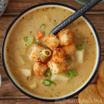 Bowl of celery root soup garnished with croutons and green onion.