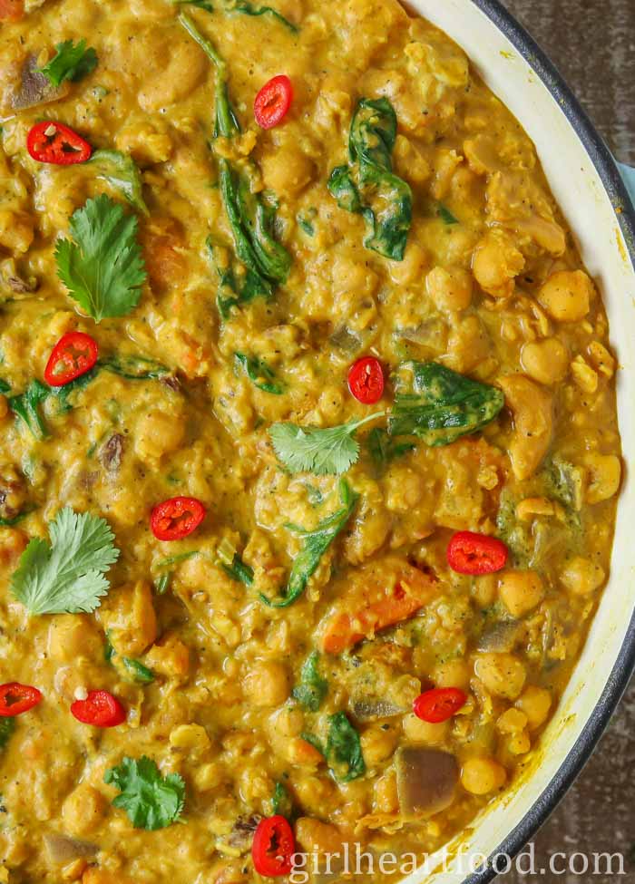 Close-up of chickpea and lentil curry in a pan garnished with sliced red chili pepper and cilantro.