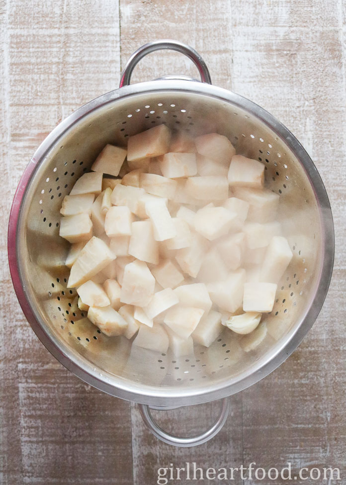 Cubes of cooked celeriac and garlic cloves in a colander.