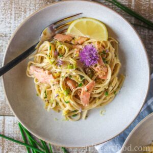 Bowl of creamy smoked salmon pasta garnished with lemon zest and chive flowers.