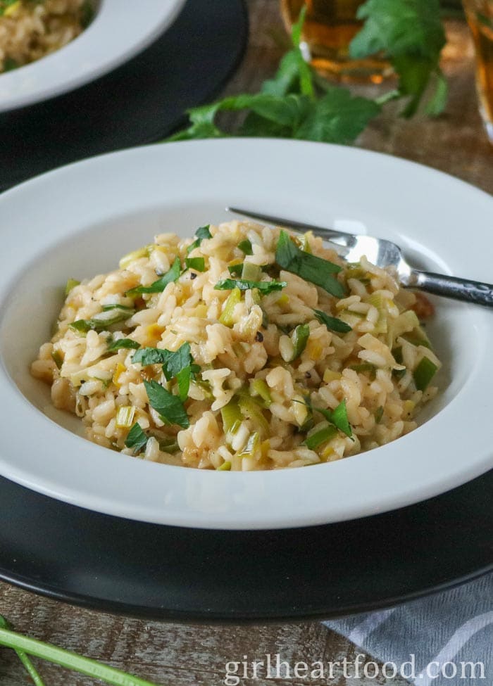 Leek risotto in a white bowl on top of a black charger plate.