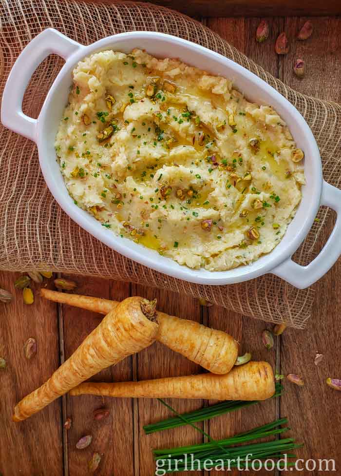 Mashed parsnips in a white dish garnished with chives, pistachios and melted butter.