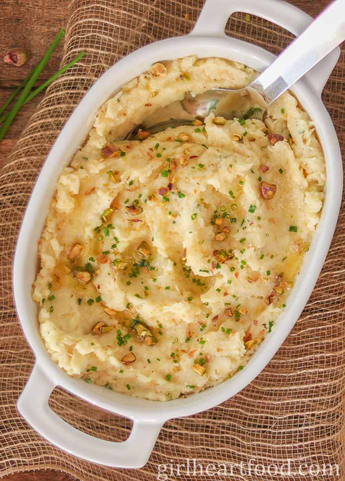 Mashed parsnips in a white dish with a serving spoon dunked into the mash.