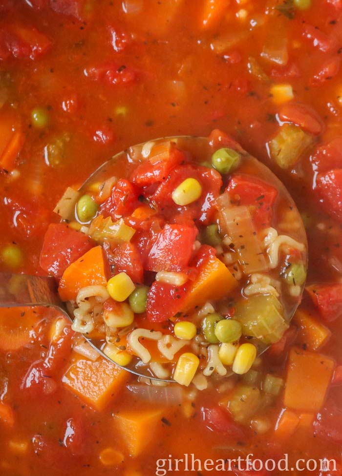 Close-up of a ladle of vegetable alphabet soup.