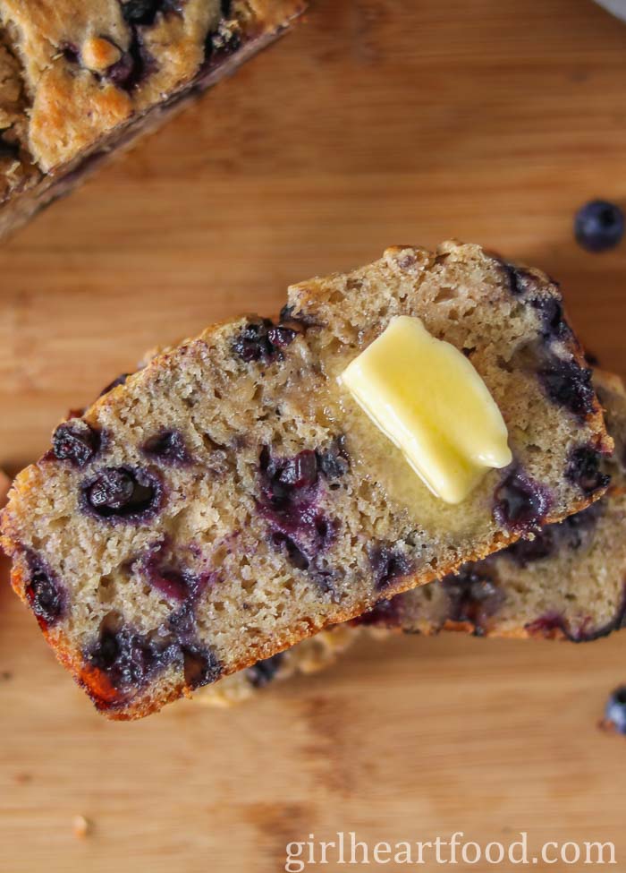 Slice of blueberry banana bread with a dab of butter on it.
