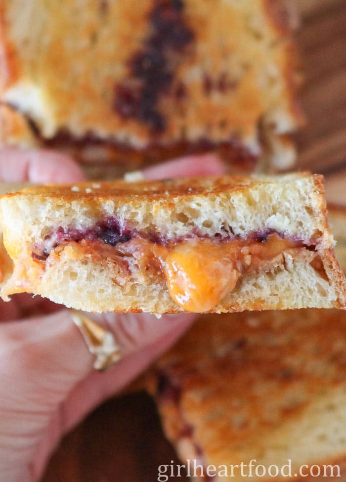 Hand holding half of a cheesy grilled pb and j sandwich.