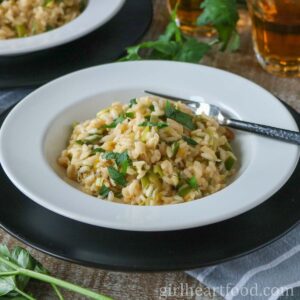 Leek risotto in a white bowl on top of a black charger plate.