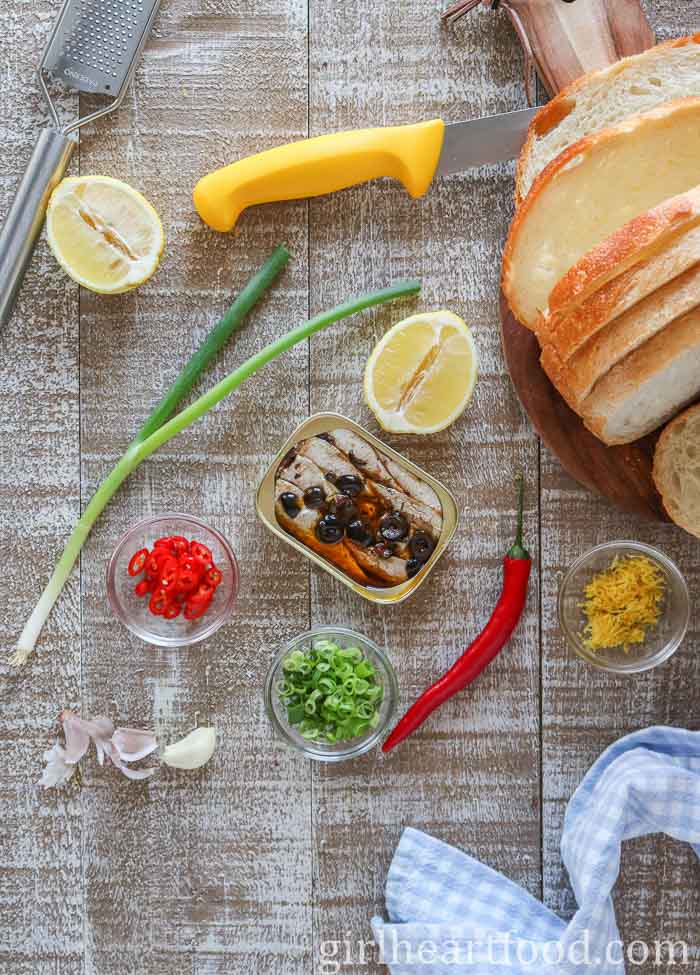 Ingredients for a canned sardine toast recipe alongside a knife, grater and tea towel.