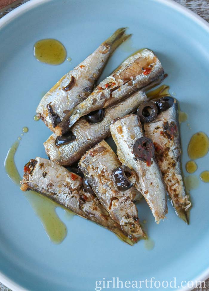 Canned sardines on a blue plate topped with olives.