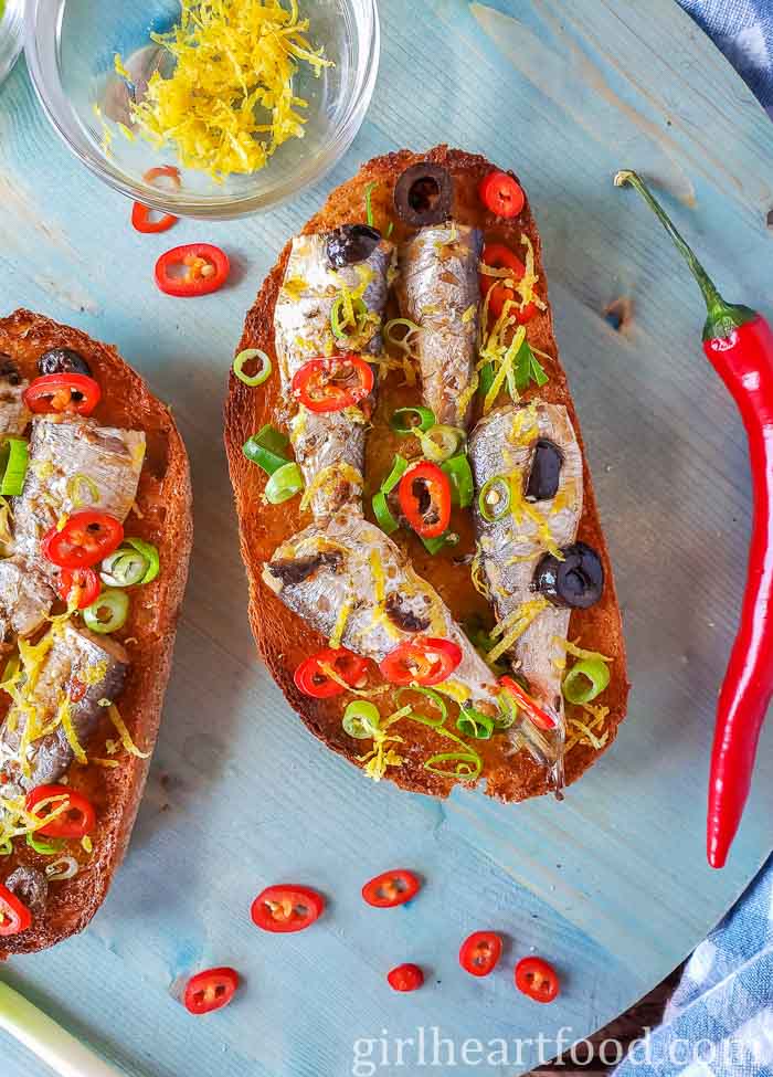 Two portions of sardines on toast with chili pepper, lemon zest and green onion.
