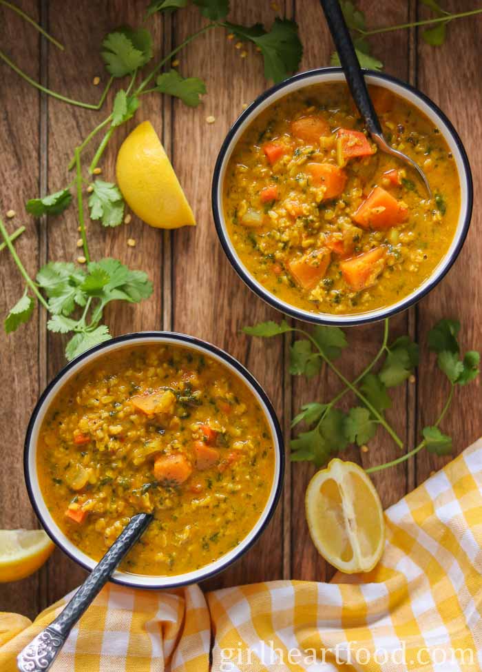 Two bowls of split mung bean soup next to lemon wedges and cilantro.