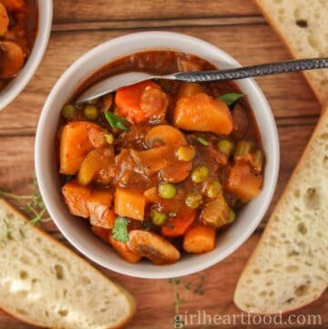 Bowl of vegetable stew, with a spoon resting in the stew, alongside slices of bread.