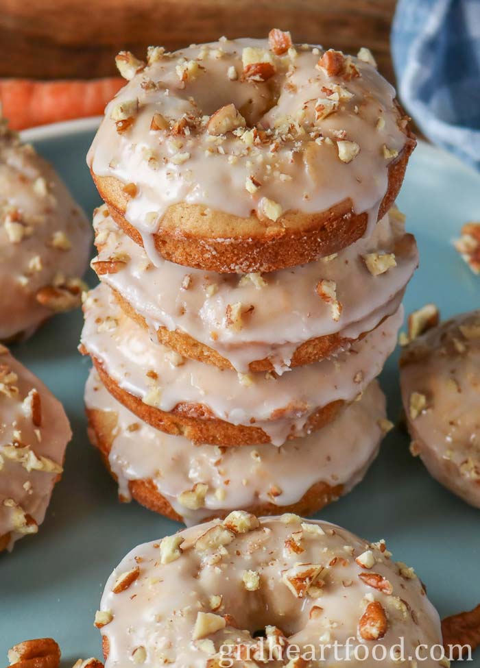 Stack of carrot cake donuts with icing sugar glaze and chopped nuts.