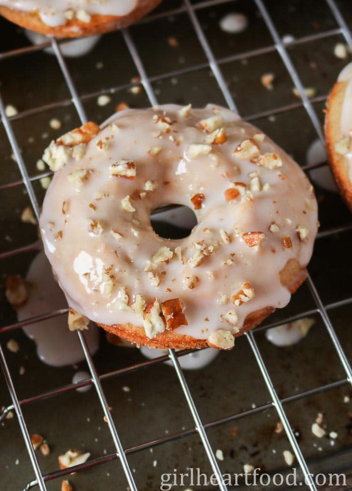 A glazed carrot cake donut with nuts on a cooling rack.