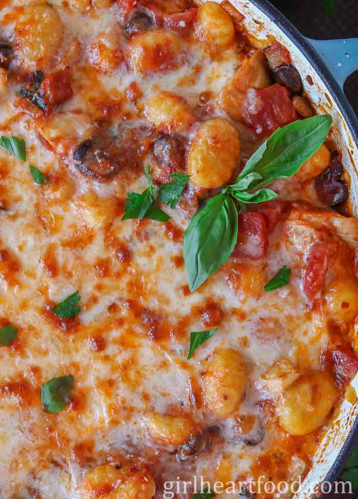 Close-up of cheesy baked gnocchi in a pan garnished with fresh herbs.