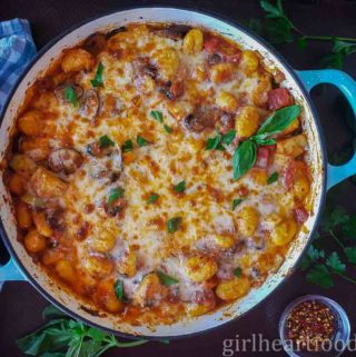 Skillet of cheesy baked gnocchi garnished with fresh basil and parsley.