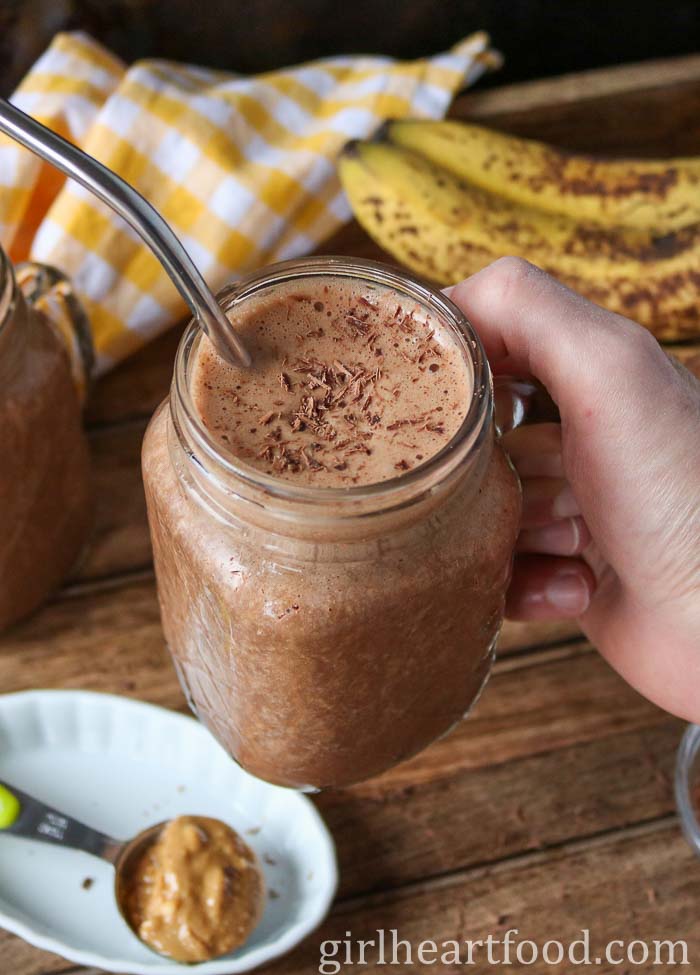 Hand holding a glass of chocolate peanut butter smoothie.