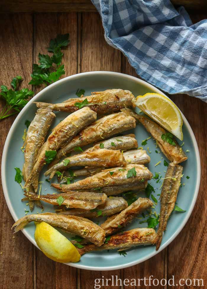 Fried smelt and two lemon wedges on a blue plate.