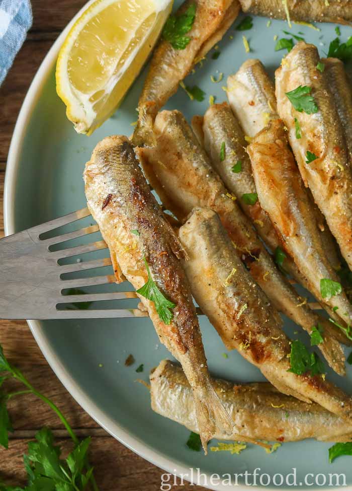 Spatula picking up pan-fried smelt up from a blue plate.