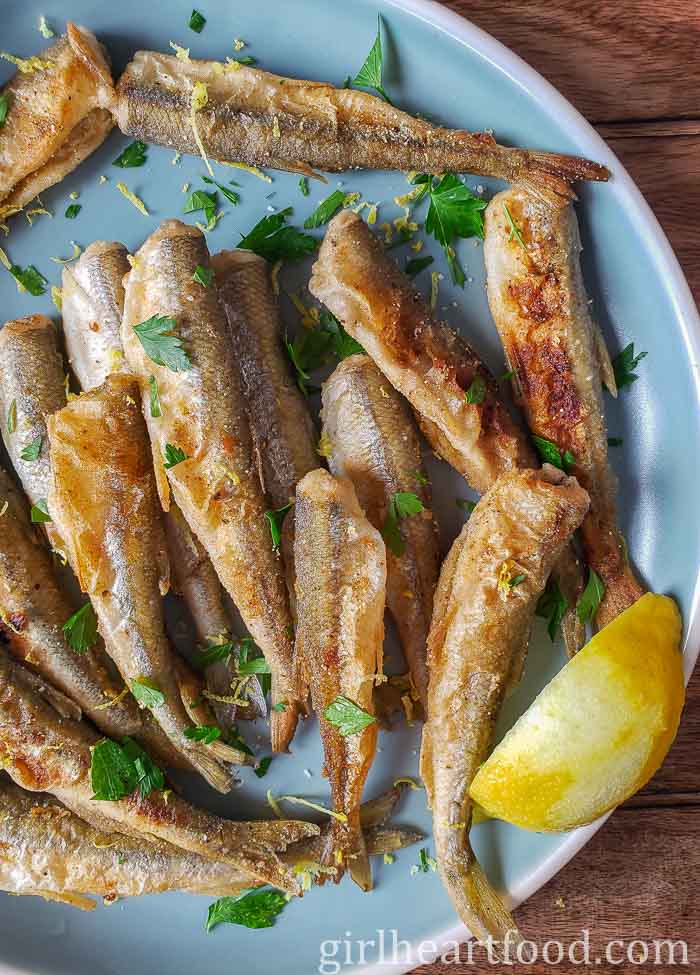 Crispy smelt fish and a lemon wedge on a blue plate.