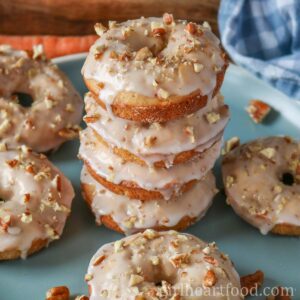 Stack of glazed carrot cake donuts on a blue plate with more donuts around it.