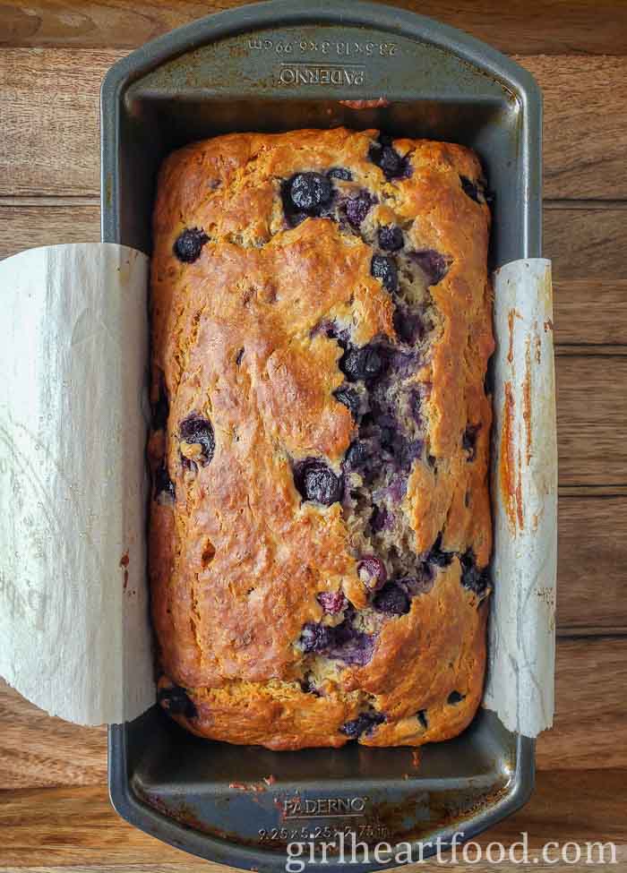 Baked blueberry banana loaf in a parchment paper-lined loaf pan.