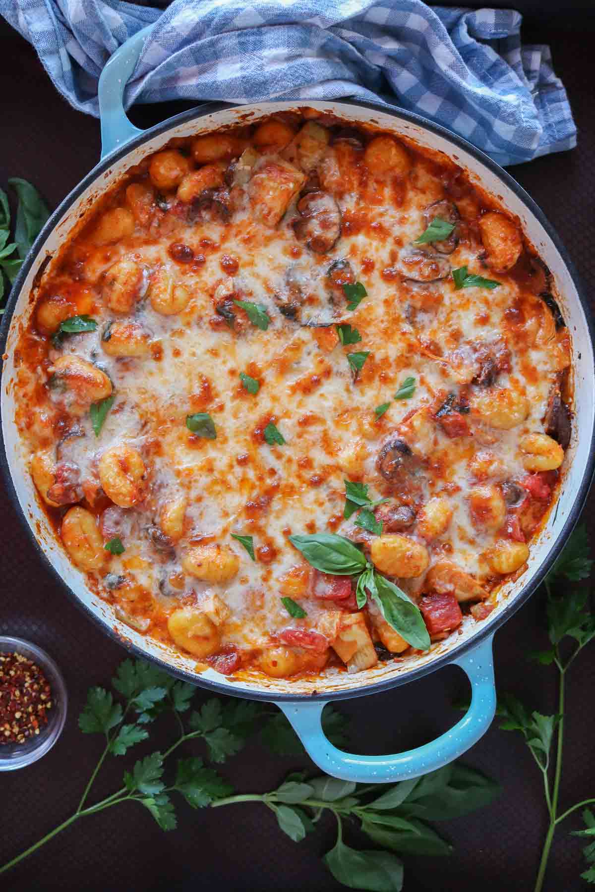 Cheesy baked gnocchi in a pan garnished with fresh basil and parsley.