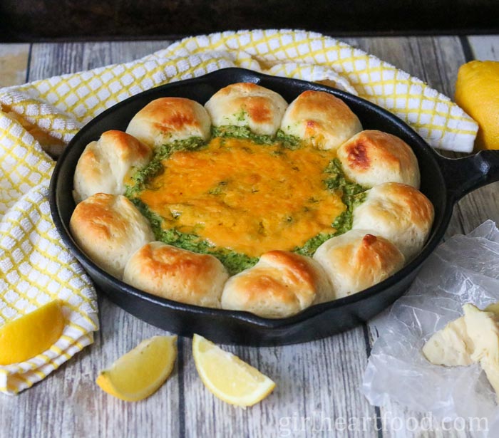 Spinach artichoke dip and biscuits in a skillet next to lemon, a tea towel & Parmesan.