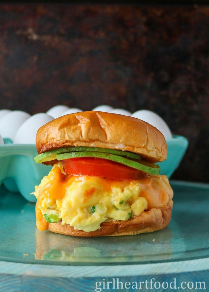 Cheesy breakfast sandwich with a container of eggs behind it.