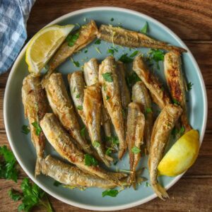 Fried smelt and two lemon wedges on a blue plate.