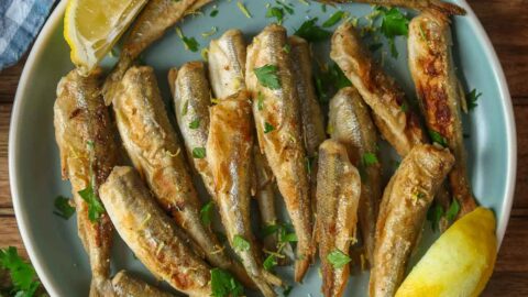 Fried smelt and two lemon wedges on a blue plate.
