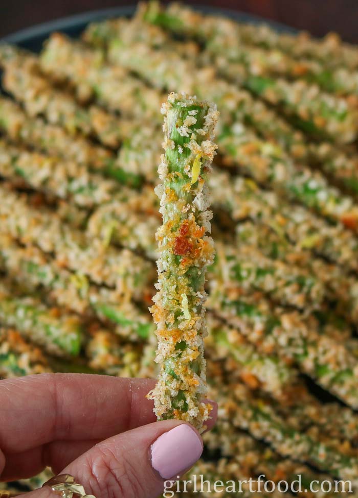 Hand holding a stalk of breaded asparagus.