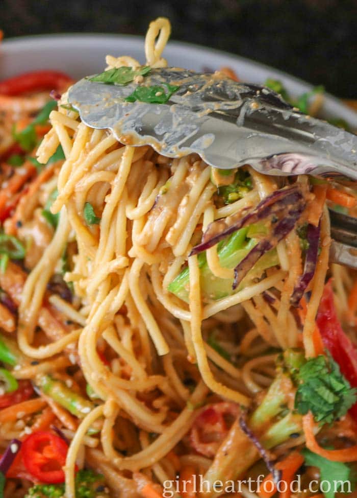 Tongs picking up some peanut noodles from a dish.