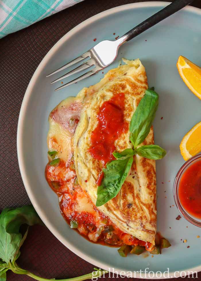 Cheesy omelette with pizza sauce and basil on a blue plate.