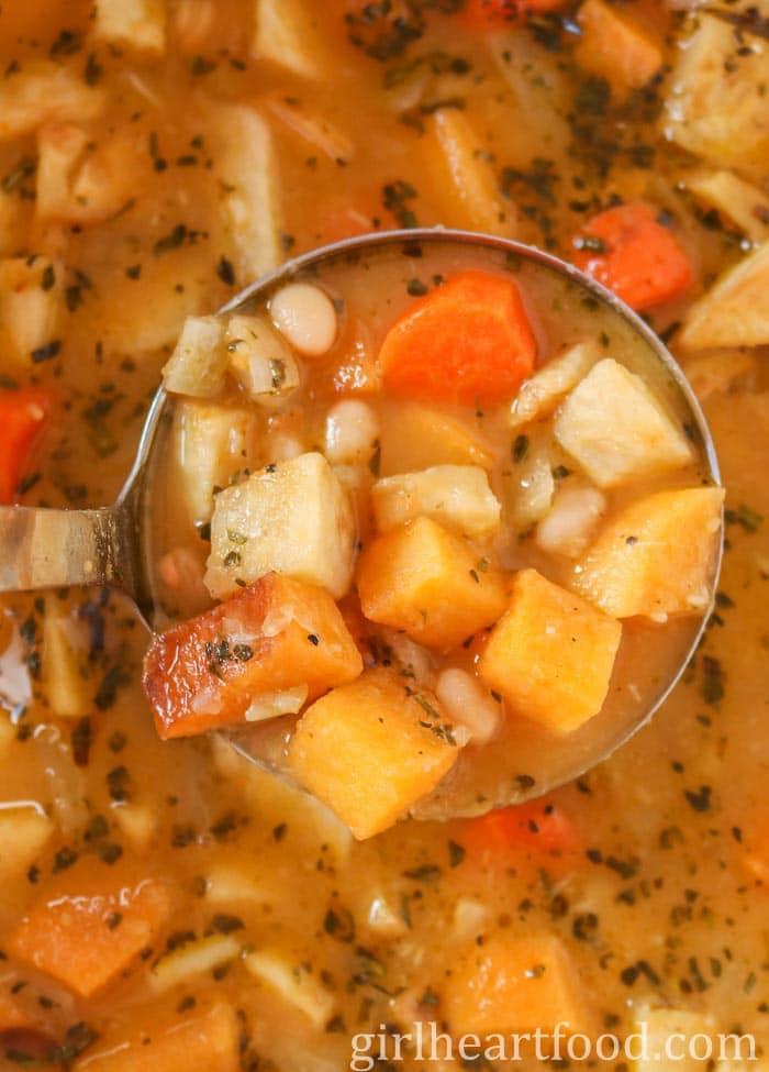 Close-up of a ladle of chunky vegetable soup.