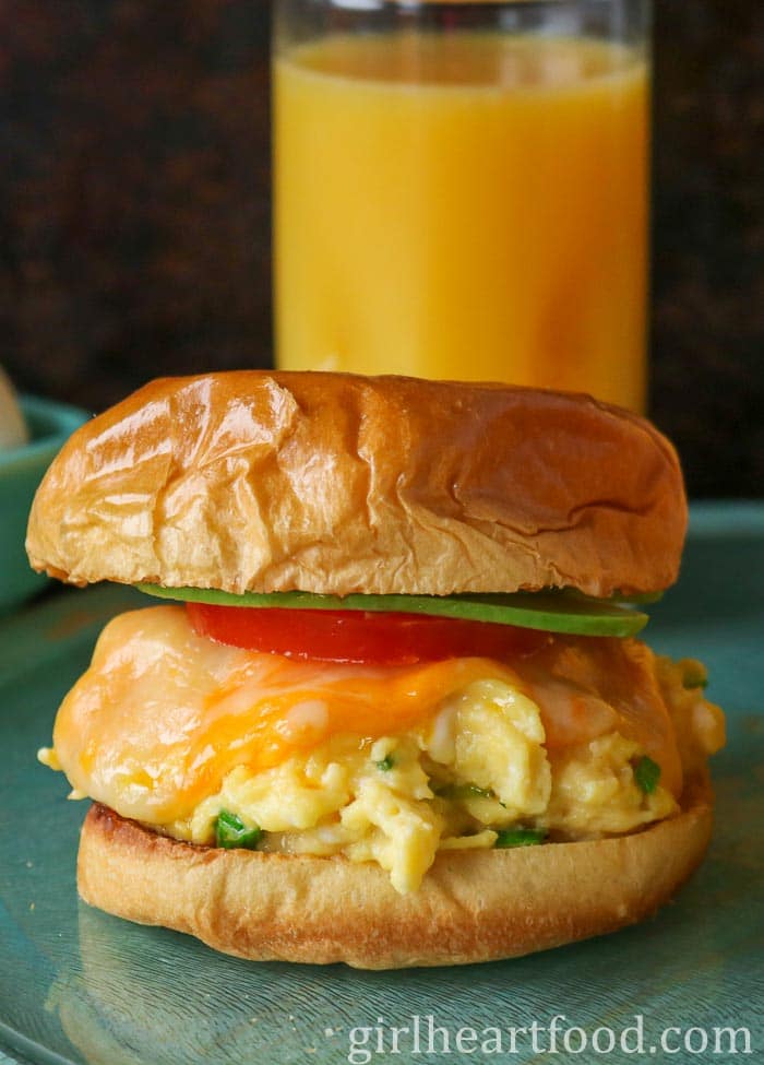 Cheesy scrambled egg sandwich with a glass of orange juice behind it.