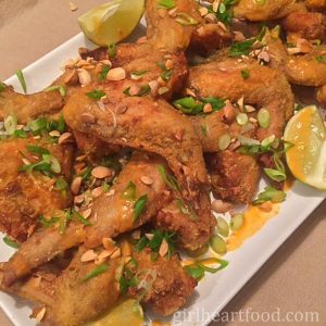 Crispy baked chicken wings garnished with green onion and nuts on a white platter.