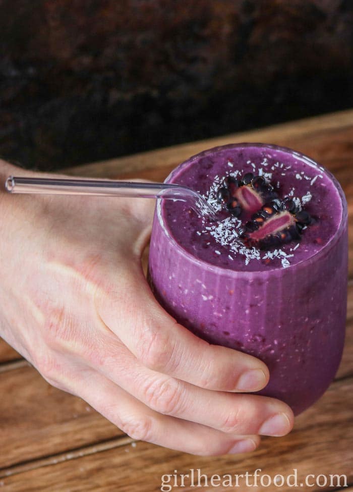 Hand holding a glass of blackberry smoothie.