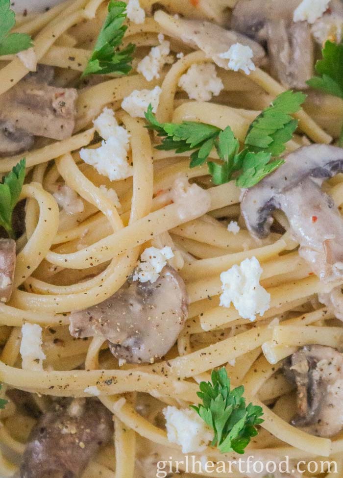 Close-up of linguine pasta with sliced mushrooms, crumbled blue cheese and chopped parsley.