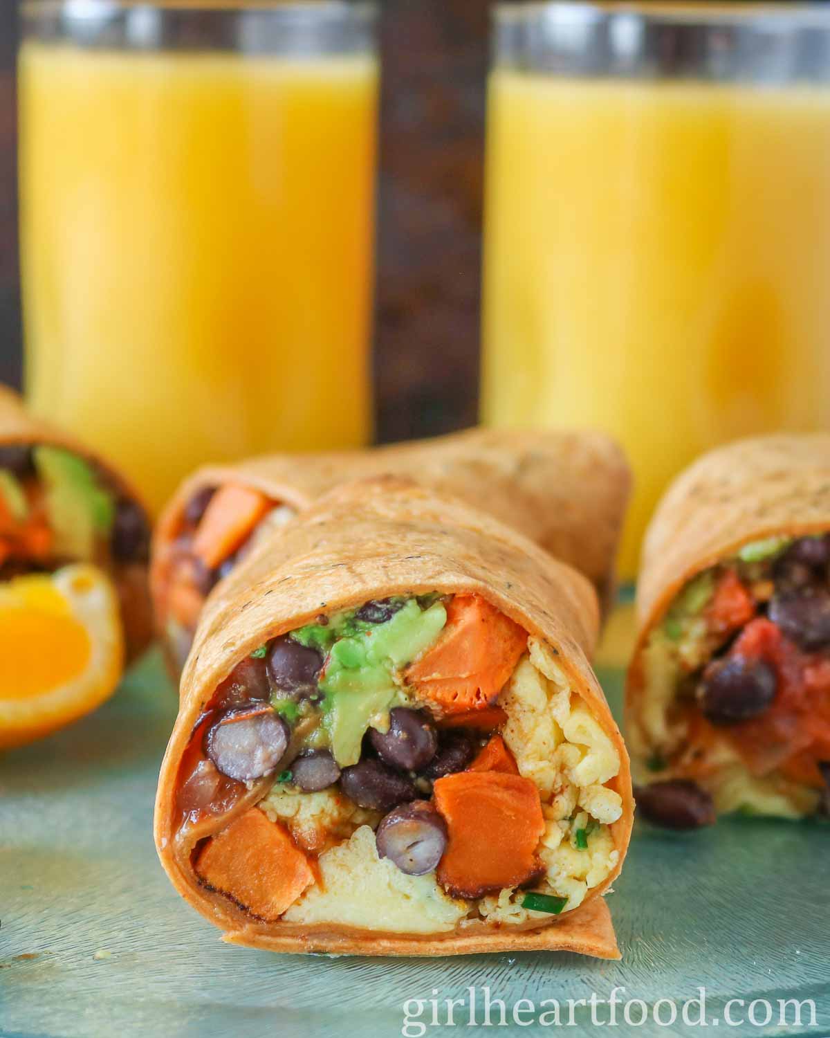 Four scrambled egg wraps in front of two glasses of orange juice.