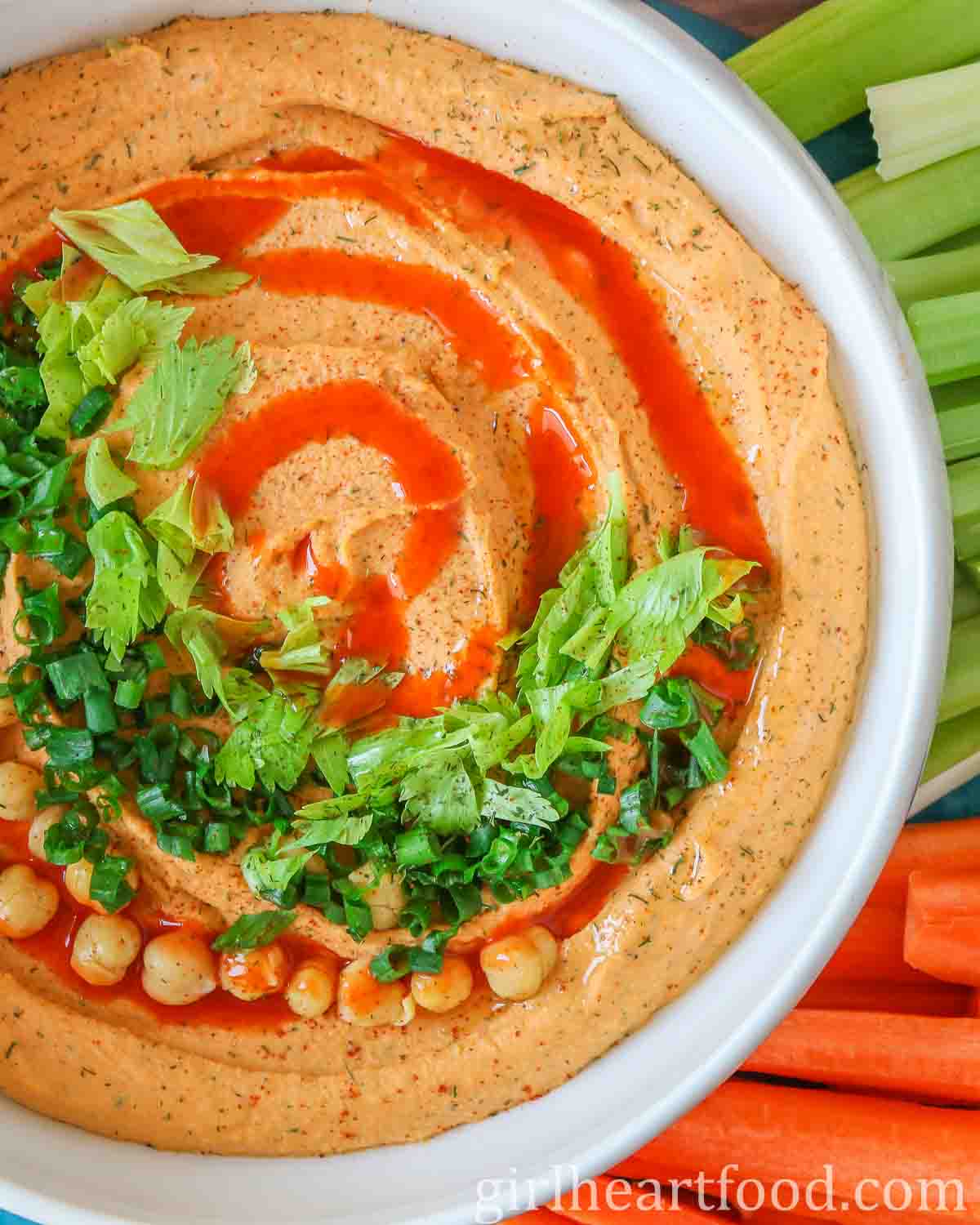 Close-up of a bowl of buffalo hummus garnished with toppings.