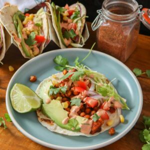 Chickpea and sweet potato taco on a blue plate with more tacos and jar of seasoning behind it.